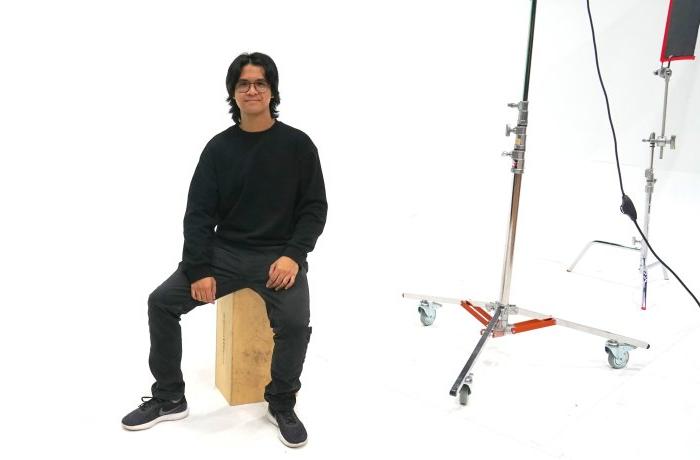 A student sits on a bench in front of a white backdrop.